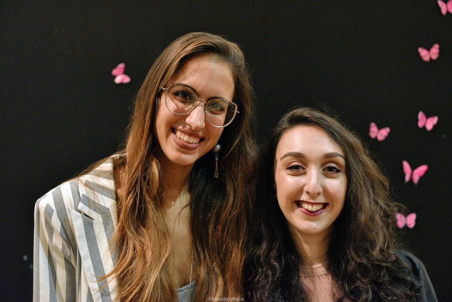 Due giovani protagoniste della serata sorridono davanti al pannello con le farfalle rosa